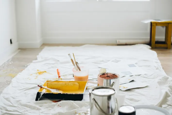 A room being renovated, paint tins on a dust sheet in front of a tall window